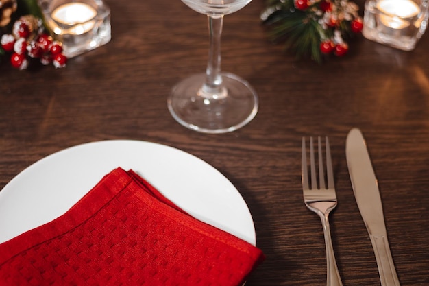 Christmas table setting Plate and cutlery on red napkin Preparing for festive dinner Candles burning on table on Christmas Eve