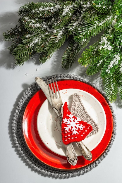 Foto impostazione della tavola di natale. piatto in ceramica rossa con posate vintage, rami di abete e accessori festivi. luce dura moderna, ombra scura. piatto creativo, sfondo grigio, vista dall'alto