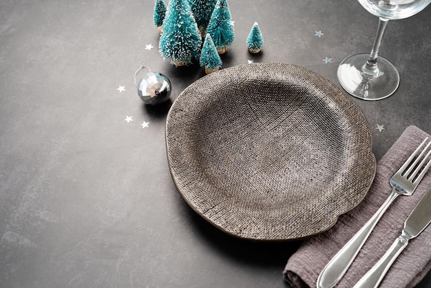 Christmas table setting with black dishware silverware and green decorations on dark background Top view