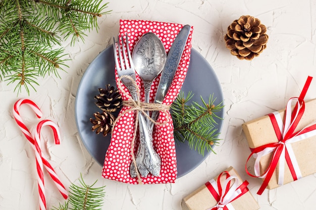 Christmas table setting with candy cane, christmas tree, pine cones and gift, on white table, top view copy space