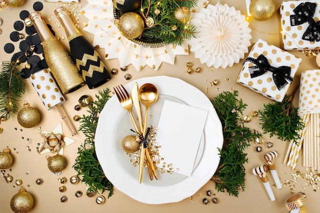 Photo christmas table setting with empty card mockup for your text. gold and black decoration with fir-tree branch. flat lay, top view.