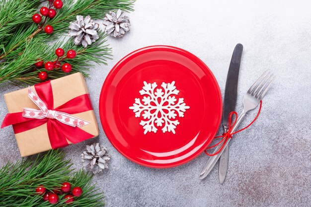 Рождественская сервировка с пустой белой тарелкой, подарком и столовыми приборами