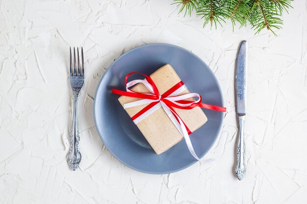 Рождественская сервировка с серой тарелкой, подарочной коробкой и столовыми приборами