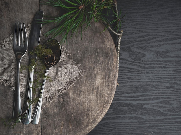 Christmas table setting with towel sackcloth and green branch as decor silverware on wooden board Top view