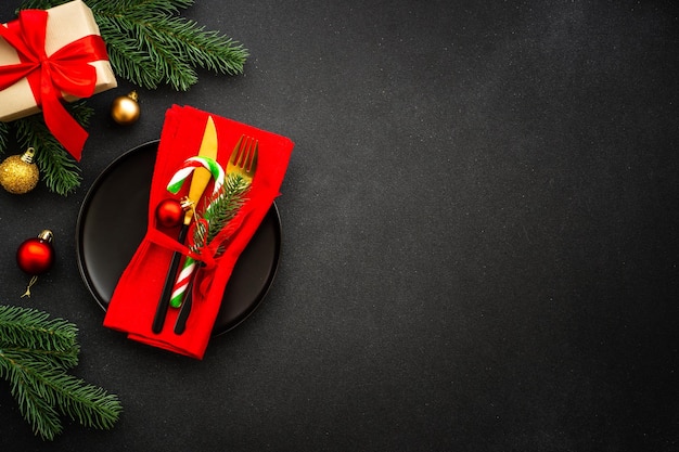 Christmas table with black plate golden cutlery and holiday decorations top view on black