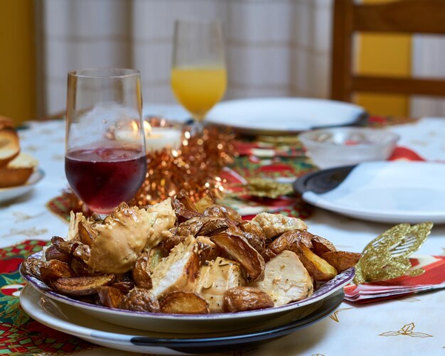 Christmas table with plate in the foreground with chicken and\
rustic potatoes, glass of wine and christmas decorations