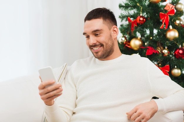 Concetto di natale, tecnologia, persone e vacanze - uomo sorridente con messaggio di sms smartphone a casa