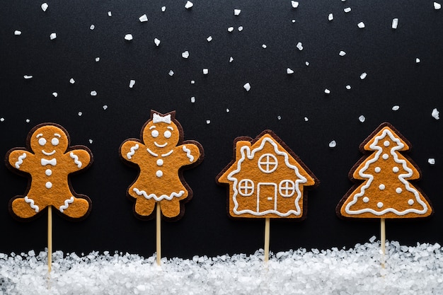 Christmas Theme. Ginger Men (Male, Female) In The Snow (Large Sea Salt) Next To The House And Tree. Close-Up.