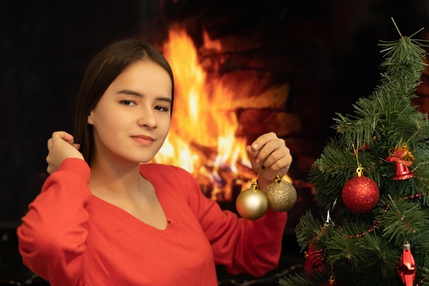 Foto tema natalizio una giovane donna decora un albero con giocattoli sullo sfondo di un camino