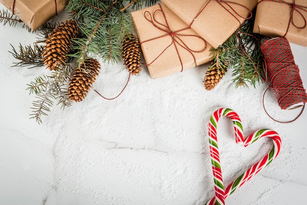 Christmas time concept, Christmas tree branches, pine cones, gifts and traditional New Year sweets candy cane, on a white marble table with snow.  copyspace top view