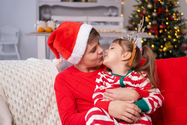 Christmas time. cute kids brother and sister in christmas\
pajamas hugging together on couch