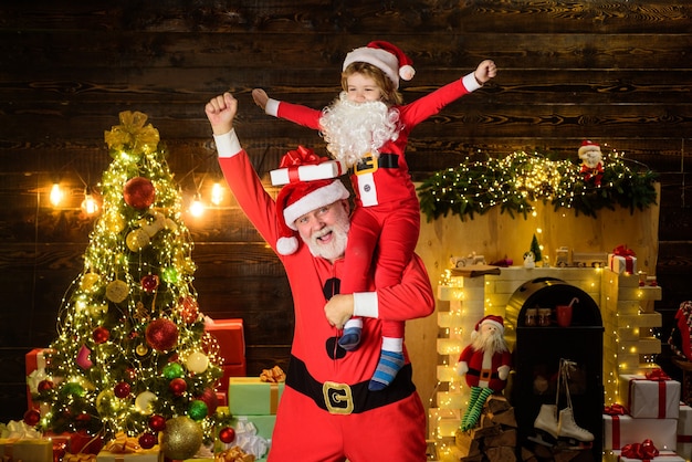 クリスマスの時期の小さな子供はサンタクロースの肩に家族の休日と子供の頃の概念に座っています