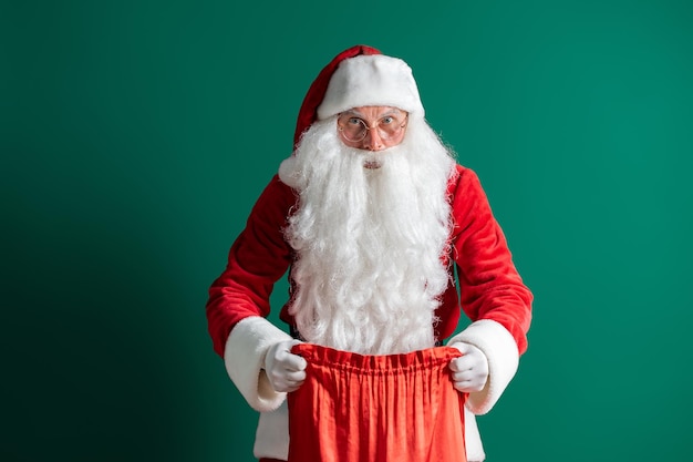 Christmas time santa claus holds and opens a bag of gifts on green background new year concept