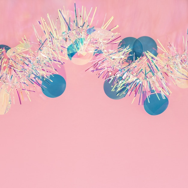 Christmas tinsel garland and confetti border on pink copy space background.