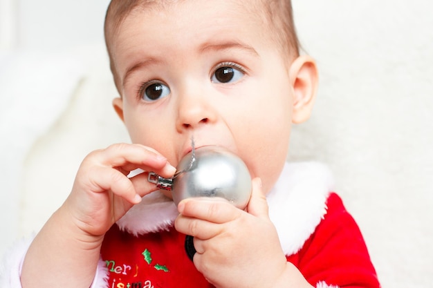 口の中で銀のボールのおもちゃで遊ぶクリスマスの幼児