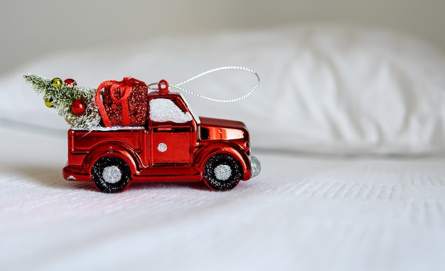 白いベッドの上のクリスマスのおもちゃの車。ハッピークリスマス、新年、休日、冬、挨拶の概念。