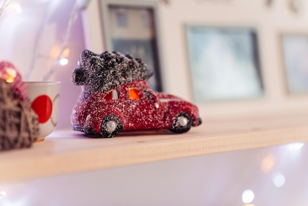 Photo christmas toy figurine red car with christmas tree on roof in snow figurine is on shelf copy space