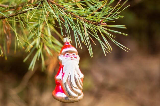 Christmas toy red Santa Claus on a natural branch with pine tree needles in the snow background Concept for New Year Christmas and winter holidays Xmas winter background