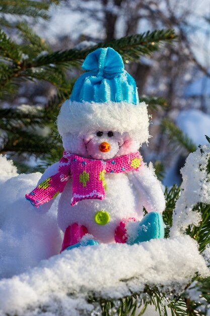 Christmas toy snowman in a blue cap sitting on the snow on the branches of the Christmas tree close up