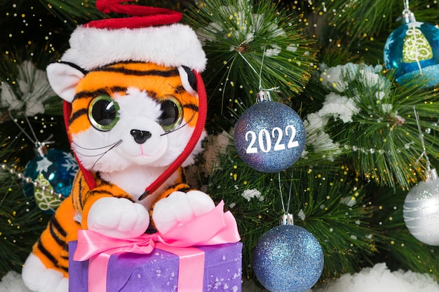 Foto tigre giocattolo di natale con un regalo vicino all'albero nella neve.