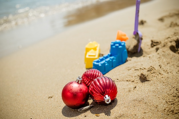 Christmas toys, decorations on the sand beach against ocean.