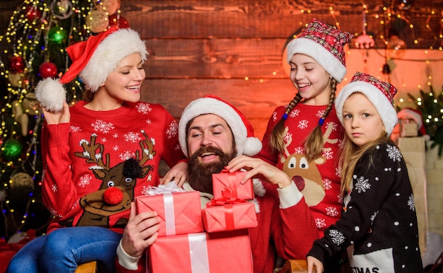 Tradizione natalizia padre uomo barbuto e madre con graziose figlie albero di natale sfondo buone vacanze trascorri del tempo con la tua famiglia genitori e figli che aprono i regali di natale santo stefano