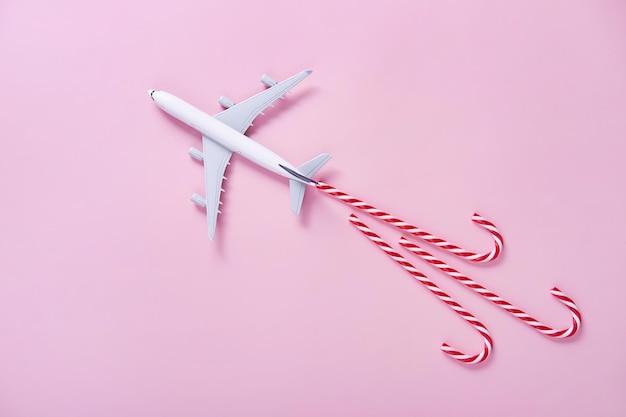 Christmas travel concept Model of passenger plane and candy canes on pink background