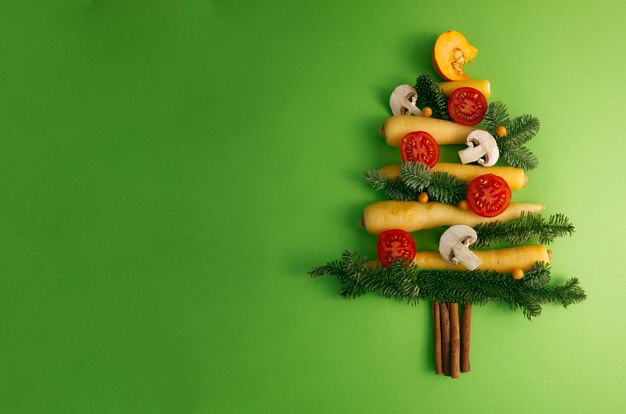 Christmas tree assembled from vegetables tomatoes, carrots, mushrooms on a green background top view