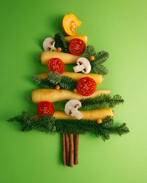 Christmas tree assembled from vegetables tomatoes, carrots, mushrooms on a green background top view