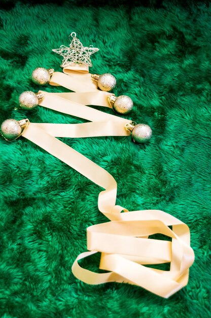 Christmas tree being made with golden satin ribbon balls and star made of wire on slightly blurred plush green background