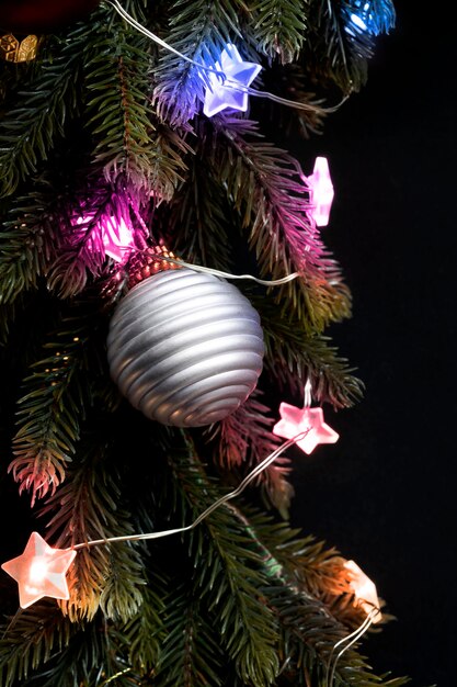 暗闇の中でカラフルなライトとボールのクローズアップとクリスマスツリーの枝