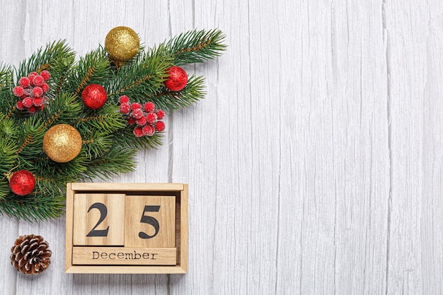 Christmas tree branch with toys and gifts and wooden calendar\
december 25 on wooden background