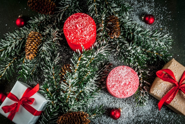 お祝いの赤いリボン、松ぼっくり、ギフトボックス、キャンドル、暗い青色の背景に雪の影響でクリスマスツリーの枝