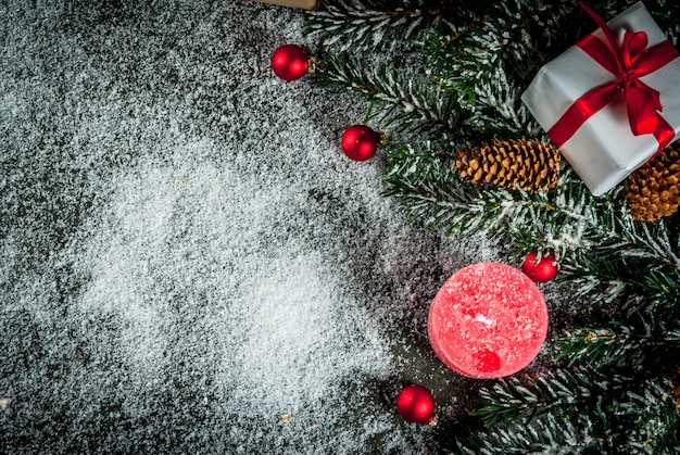 Rami di albero di natale con effetto neve con nastro rosso festivo, pigne, scatole regalo e candele, su sfondo blu scuro