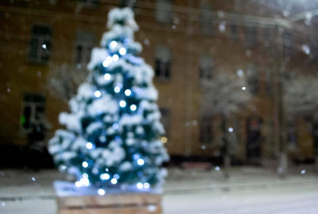 Christmas tree covered snow glowing colorful lights during snowfall outdoors