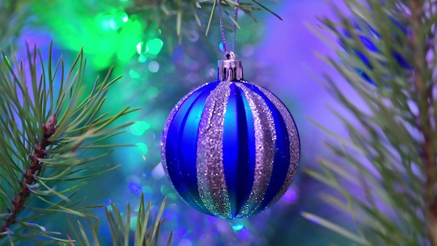 Christmas tree decorated with blue glass ball on christmas spruce branch on background bokeh of flickering light bulbs garlands