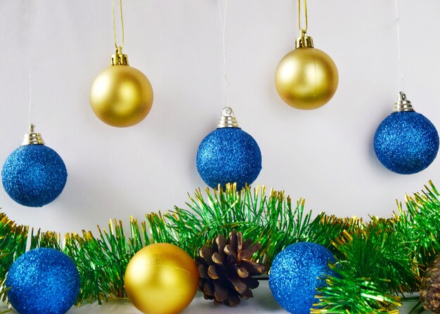 Christmas tree decorations blue and yellow balls on white wall with tinsel and cones close up.