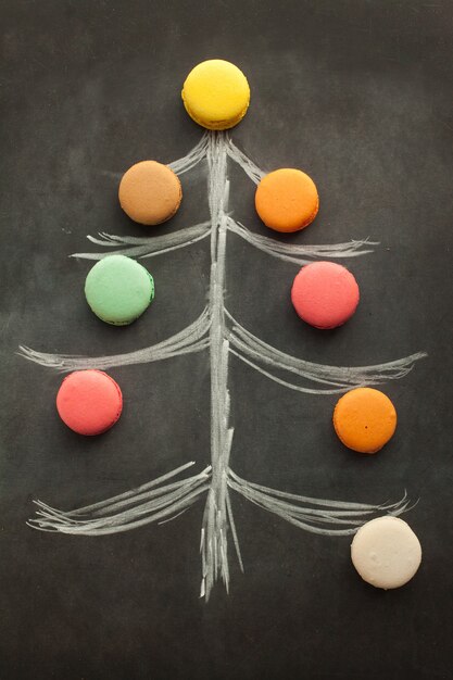 Christmas tree drawn with a piece of chalk on the chalkboard decorated with colorful macaroons