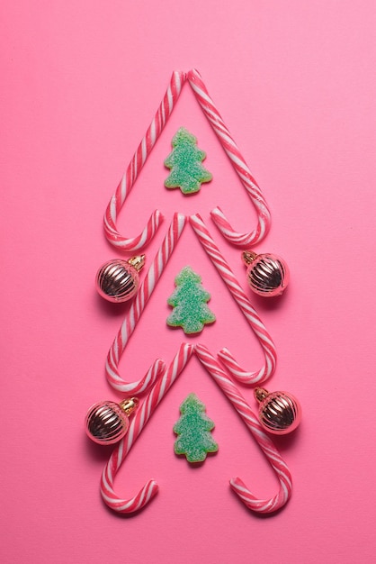 Foto figura dell'albero di natale fatta di dolci e palline decorative su una vista dall'alto di sfondo rosa