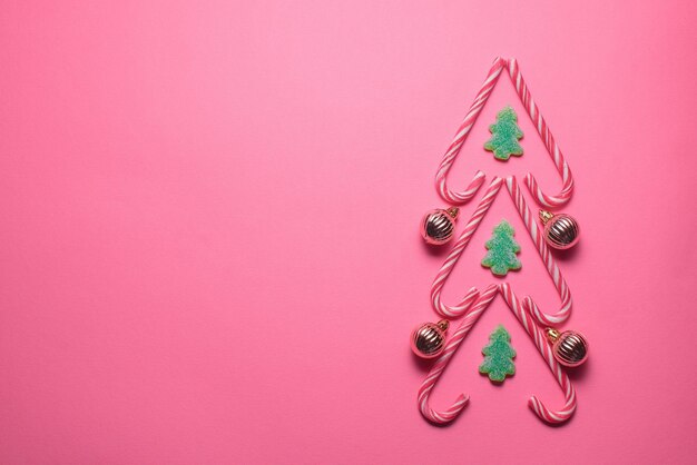 Photo christmas tree figure made of sweets and decorative balls on a pink background top view