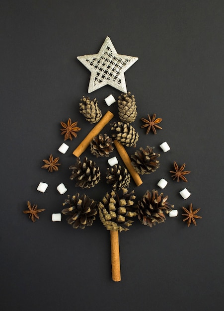 Christmas tree from pine cone, cinnamon, marshmallow and anise on the black background . Flat lay. Top view.