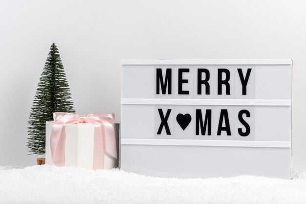 Christmas tree gift box and lightbox with text MERRY XMAS on a table with snow