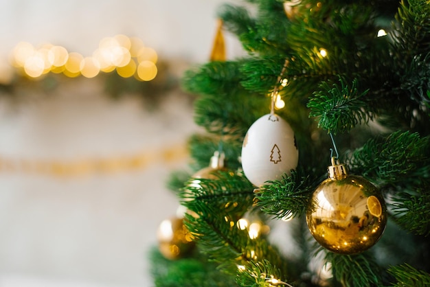 The Christmas tree is decorated with toys Golden balls white eggs and garlands in closeup