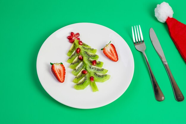 Christmas tree of kiwi and pomegranate with fork and knife