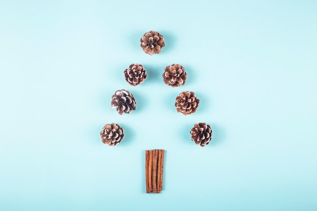 Christmas tree layout of cones and cinnamon stickson a blue background.