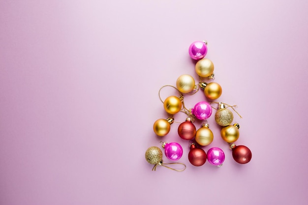 ピンクの背景にクリスマスボールで作られたクリスマスツリー。最小限のスタイルの新年のバナー。