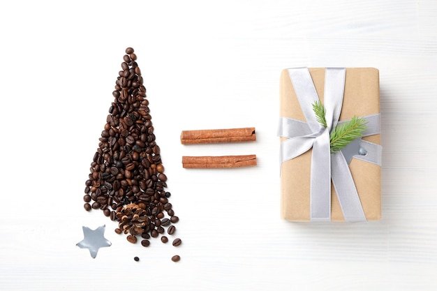 Christmas tree made of coffee beans star cinnamon and gift on white wooden background