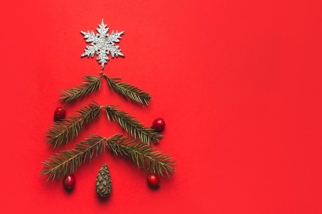 Christmas tree made of fir branches isolated on red, flat lay. New year card. Minimal New year concept.