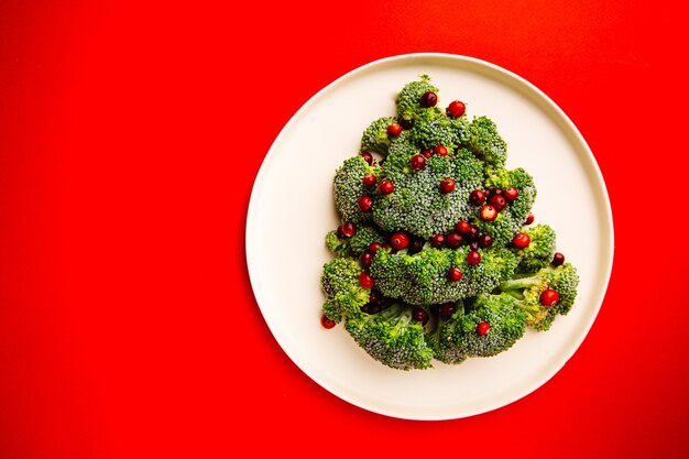 Christmas tree made from broccoli and cranberry on white plate and red background top view