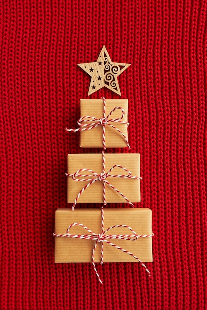 Christmas tree made of gift boxes and wooden star on red knitted background